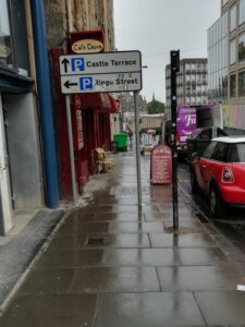 A pavement that features obstacles, including a sign and a bin which could make it difficult for disabled people to walk and wheel on.